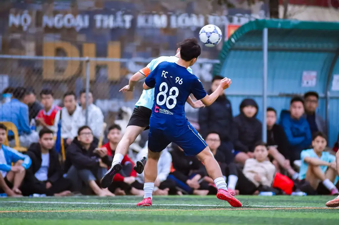 A youth footballer striking the ball during an intense match under stadium light.